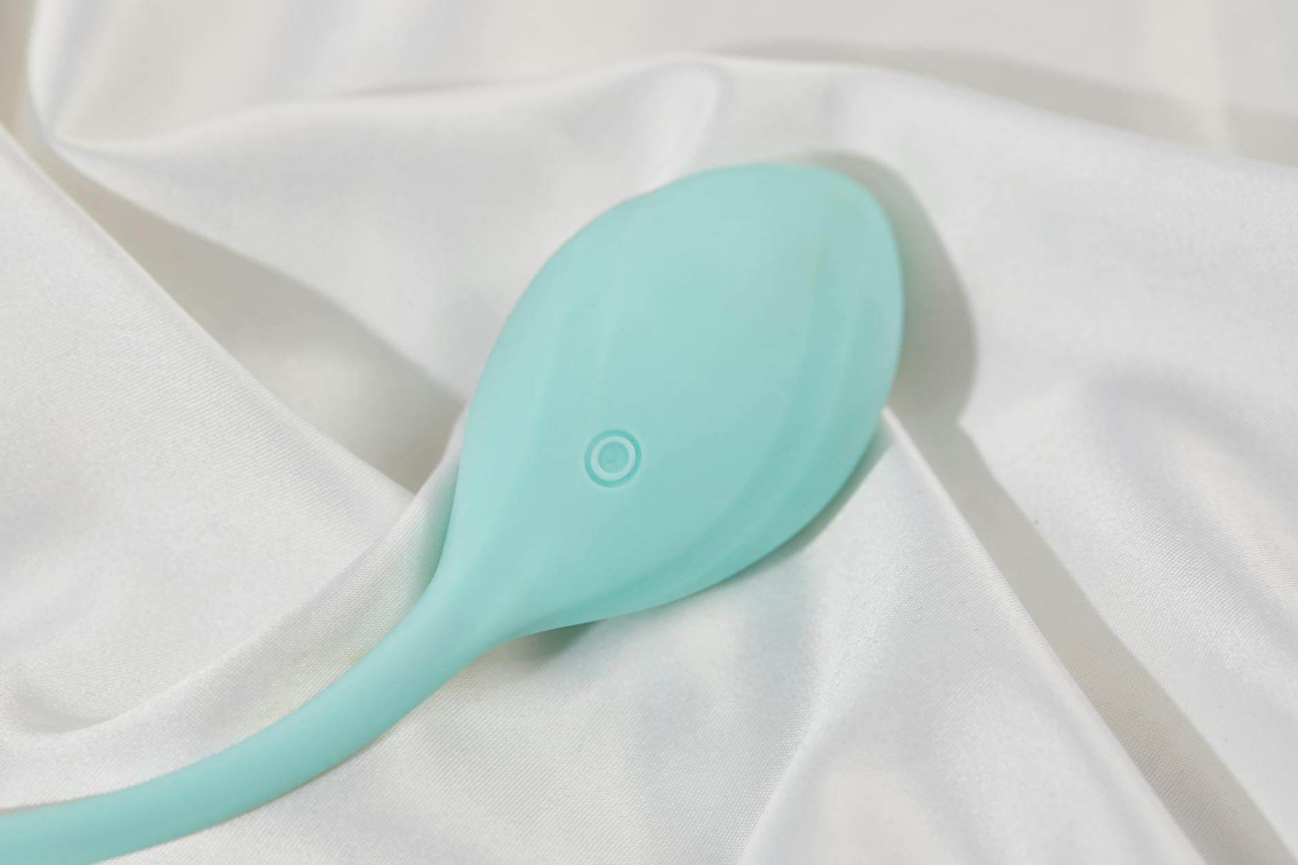 A stylish teal vibrator resting on smooth white silk fabric