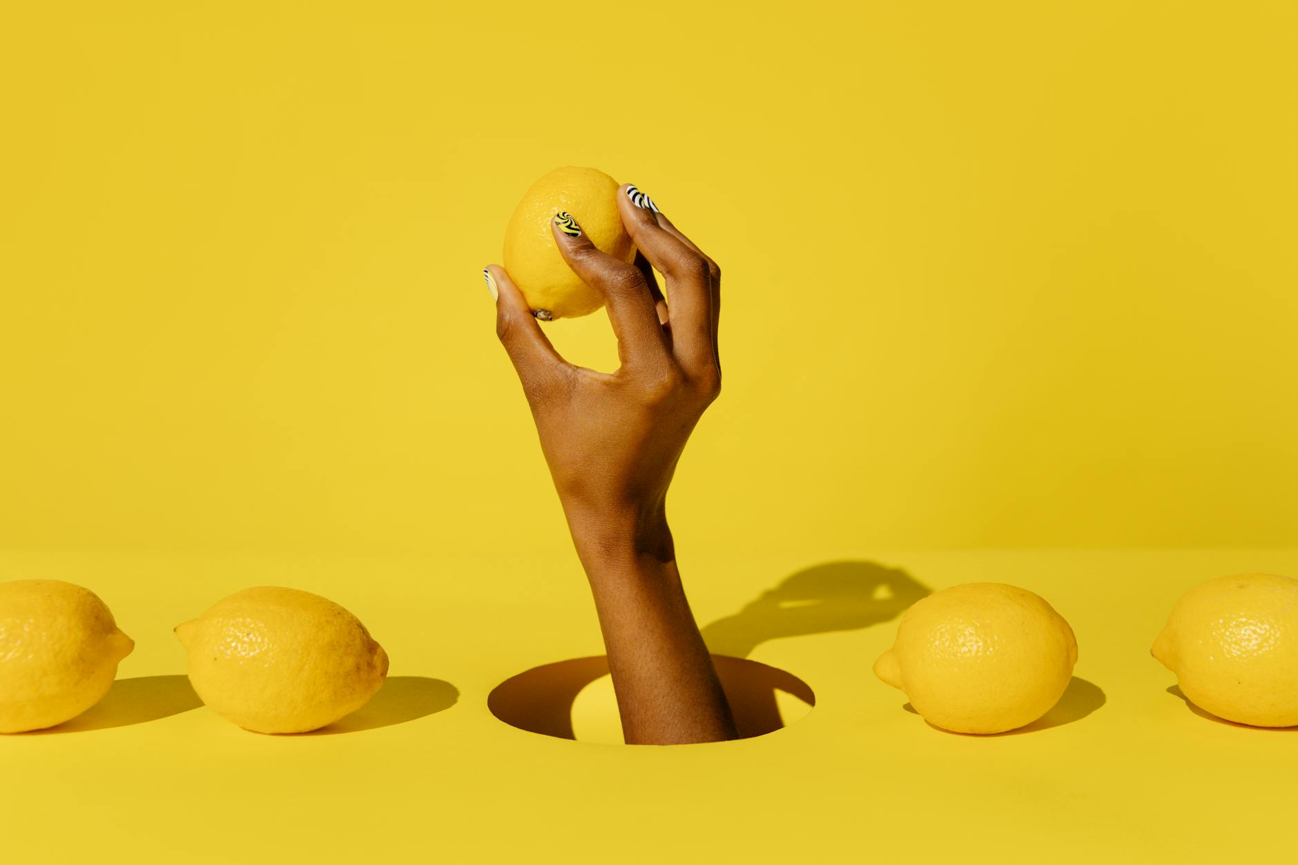 A hand holding a fresh lemon against a bright yellow background, symbolizing natural lubrication and citrus-fresh sensation.