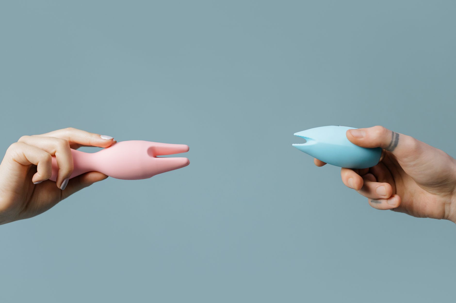 Hands holding pink and blue silicone vibrators, representing alternative pleasure options for pain-free intimacy