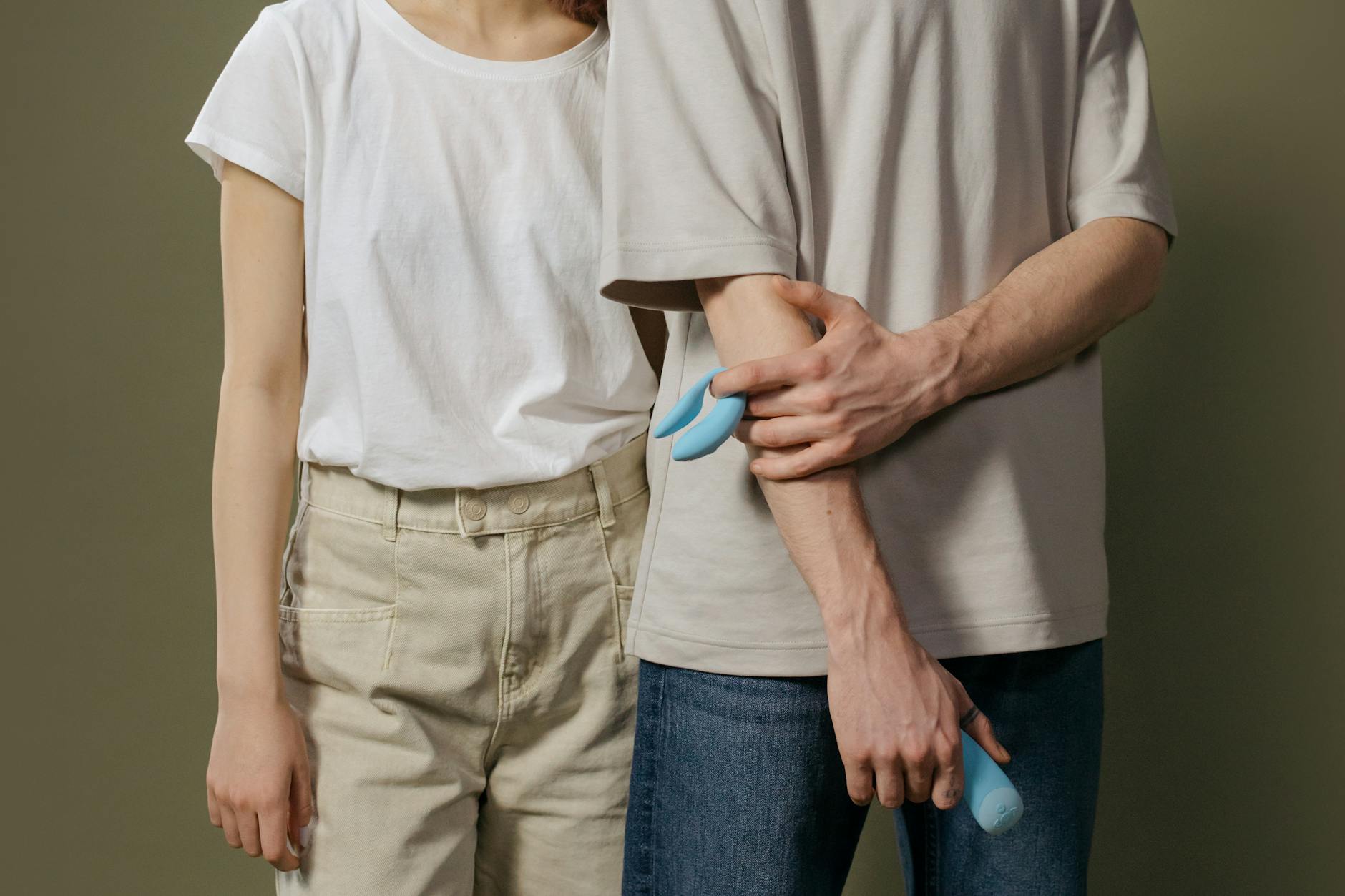 A young couple standing together indoors, holding a blue vibrator, symbolizing modern intimacy and shared pleasure.