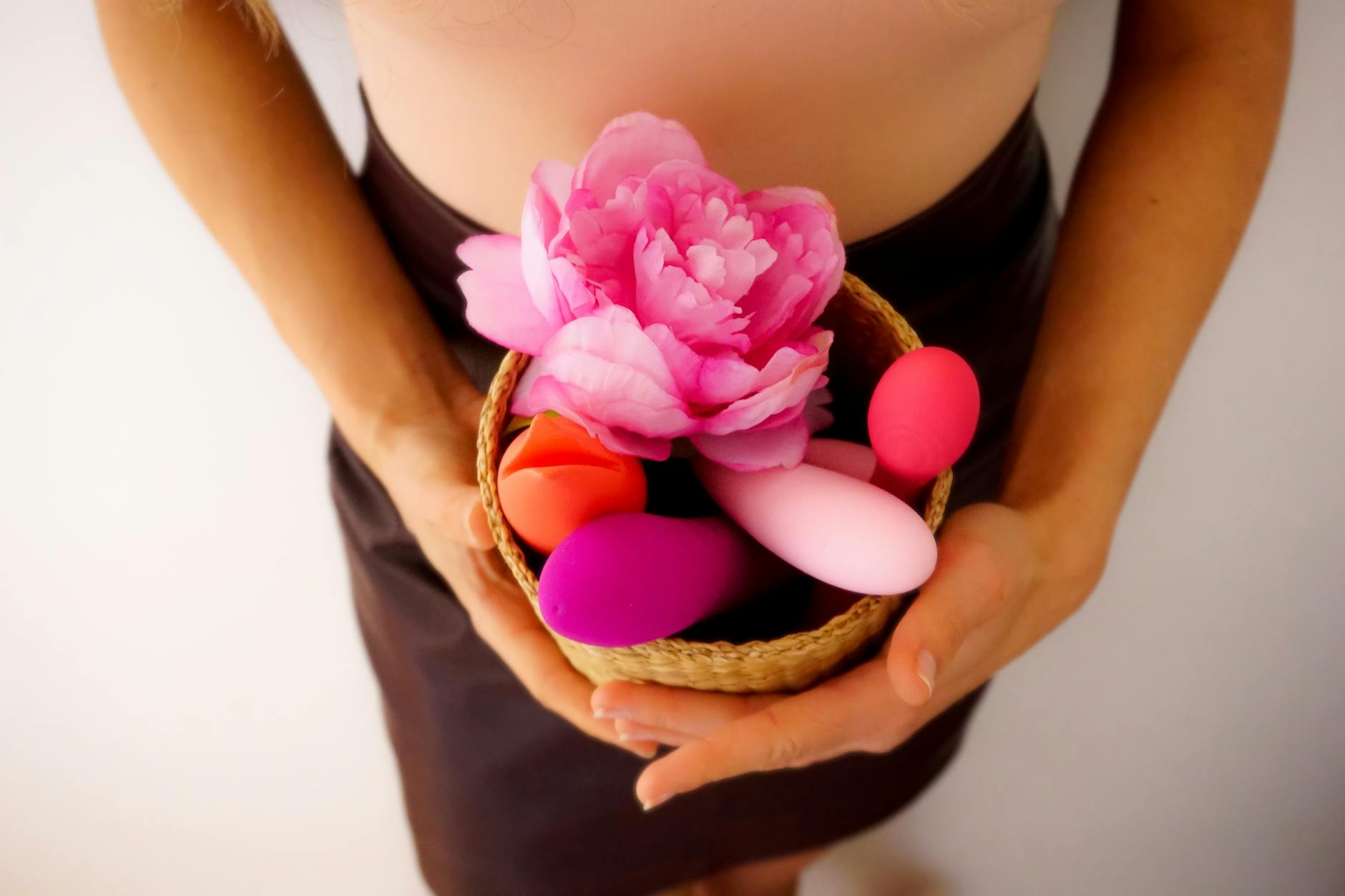 Two hands holding pink and blue clitoral vibrators against a pastel background